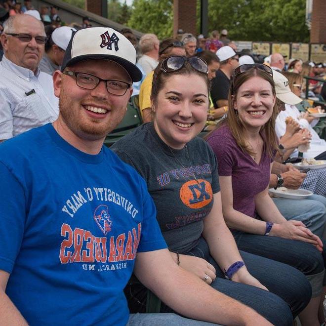 Three alumni smiling at a baseball game.