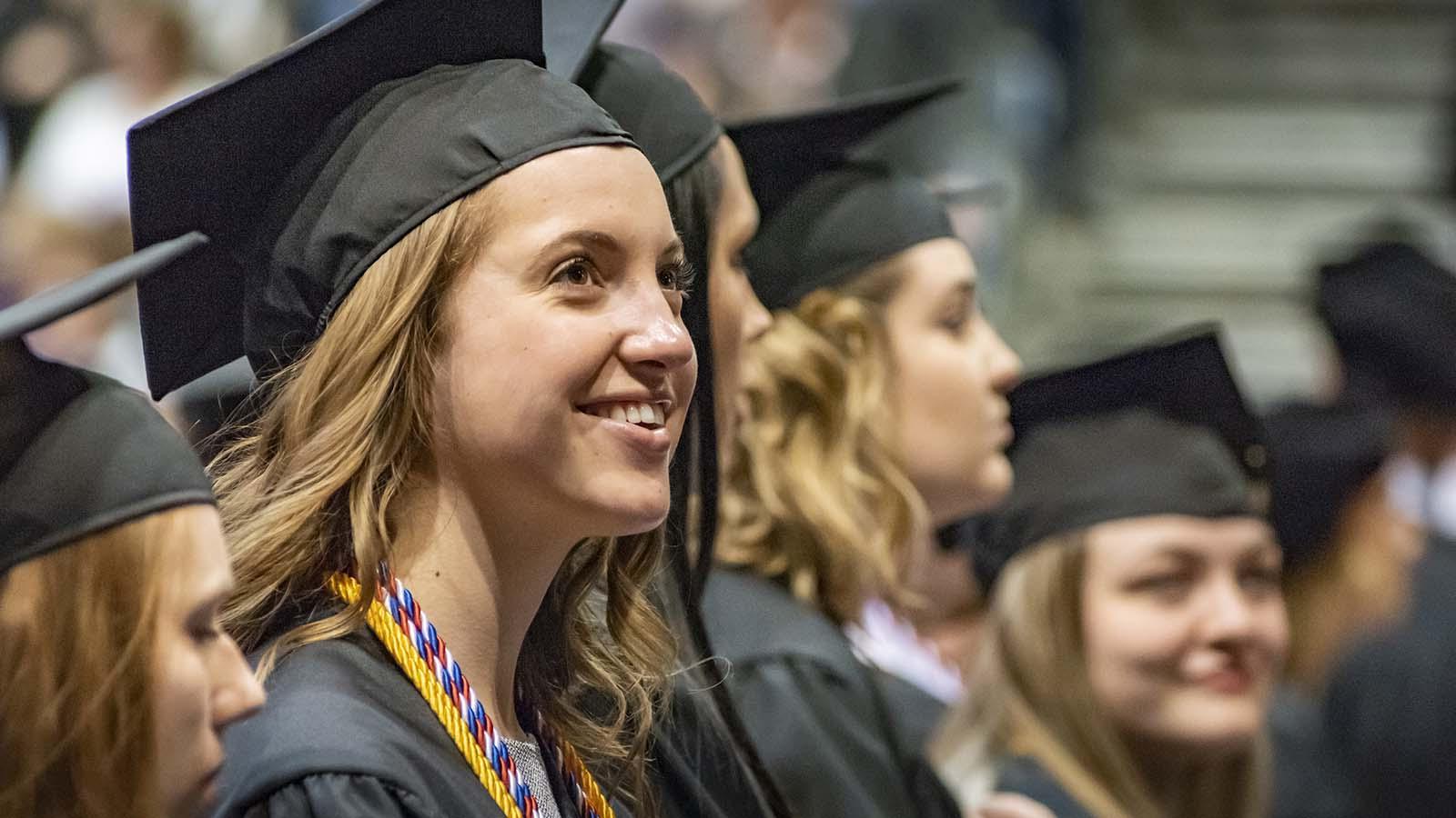 快乐的女毕业生在毕业典礼上，后面有几个学生.